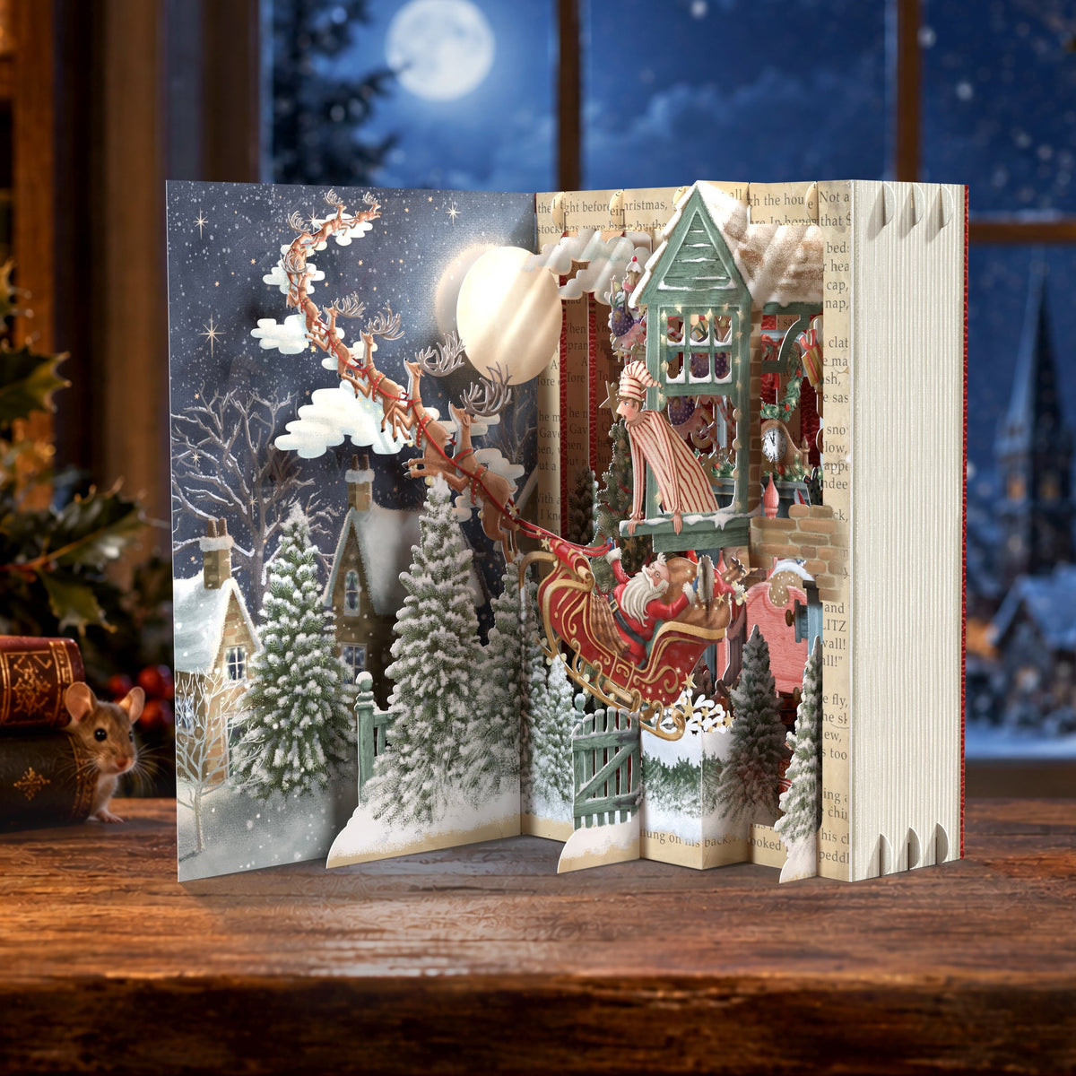 A 3D pop-up cardboard advent card featuring a festive Christmas village scene with Santa Claus in a sleigh, snow-covered trees, and a cozy house, displayed on a wooden table in a warmly lit holiday room.